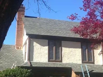 Tudor-style stucco home with a gray shingle roof and brick chimney